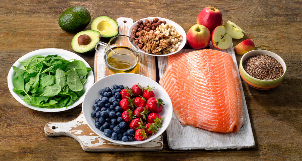 spinach, salmon, berries, avocados and a few other foods displayed on a wooden table