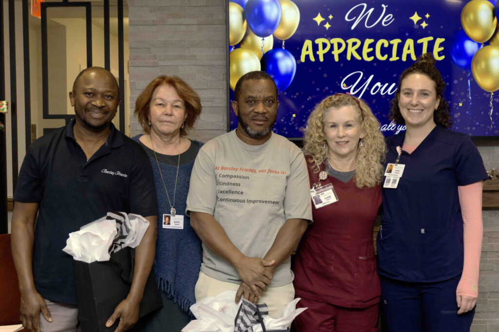 Five employees standing in a row in front of a tv screen that says we appreciate you.